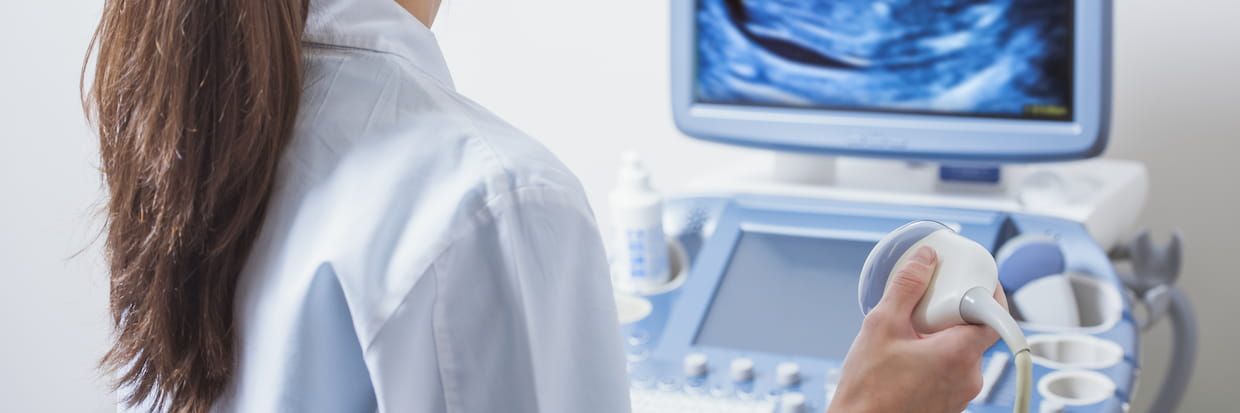 A healthcare professional in a lab coat operates an ultrasound machine, focusing on the monitor displaying an ultrasound image from sonography school.